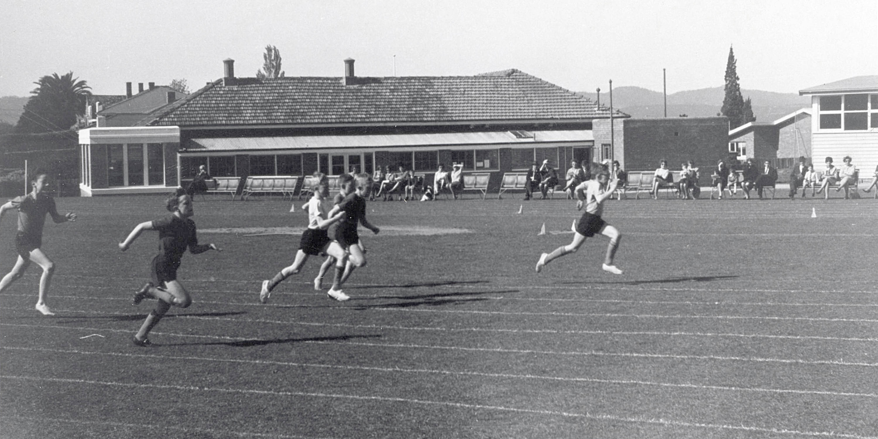 R Bingham wins U11 100yds with former Sub-Primary block (now Middle School) behind, 1960.