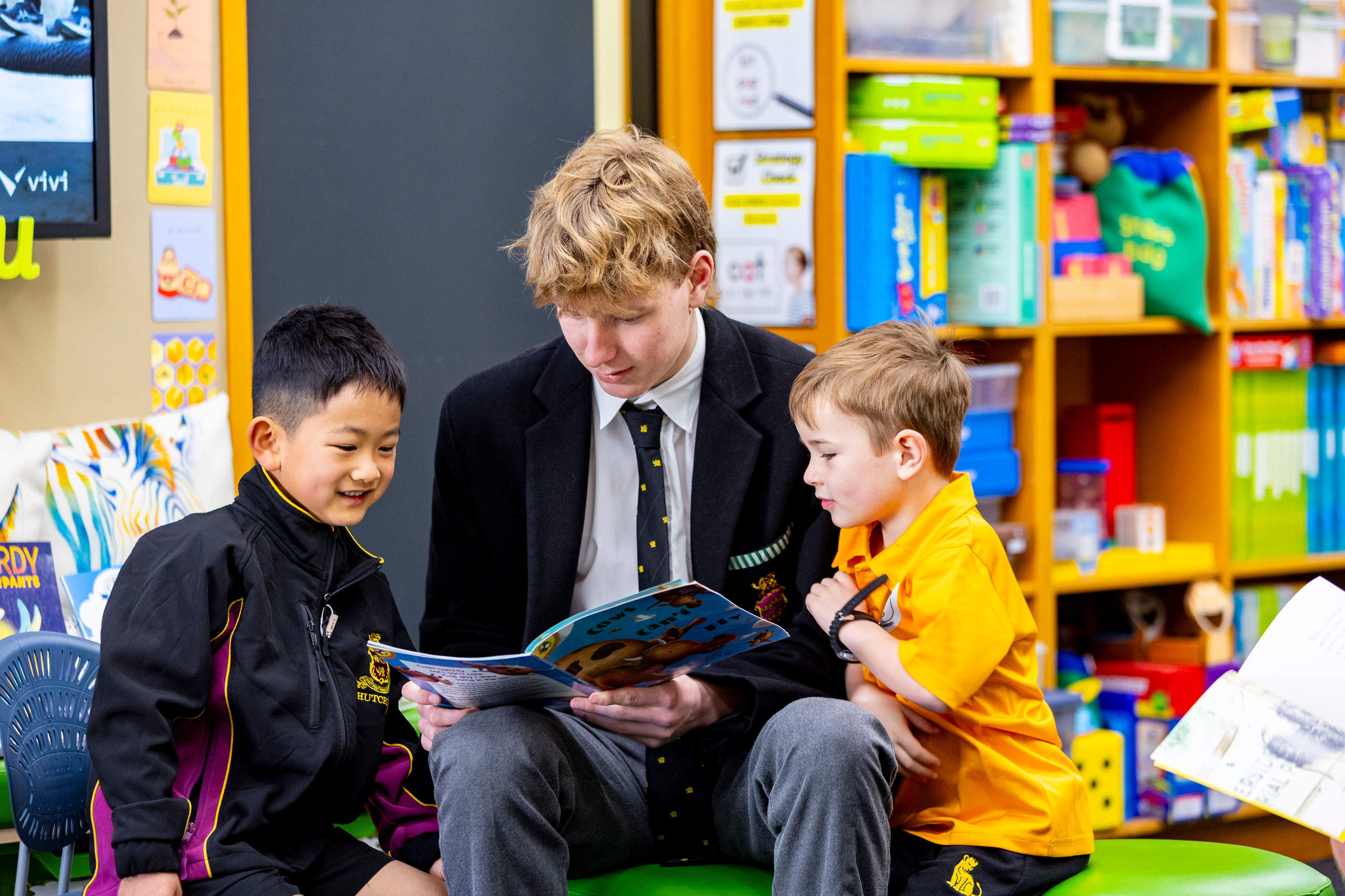 An older student reading to two younger students in a library.